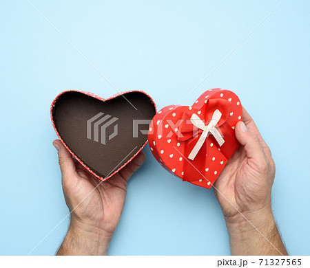 male hand holding a red cardboard box with a bow on a blue background male hand holding a red cardboard box with a bow on a blue background 71327565