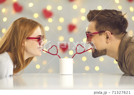 Cute happy young couple sipping drink from one cup on their date on Valentine's Day Cute happy young couple sipping drink from one cup on their date on Valentine's Day 71327621