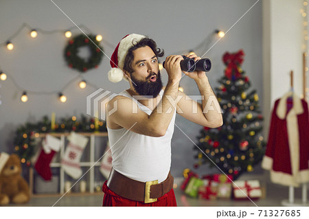 Surprised funny young Santa with binoculars looking at amazing Christmas sales and deals Surprised funny young Santa with binoculars looking at amazing Christmas sales and deals 71327685
