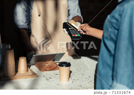 Client pays to coffee bill, millennial african american bartender in apron gives terminal in cafe counter with equipment Client pays to coffee bill, millennial african american bartender in apron gives terminal in cafe counter with equipment 71331674