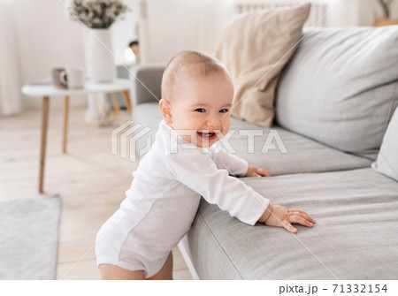 Cute Little Baby Smiling To Camera Standing Near Couch Indoor 71332154