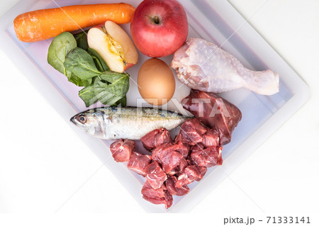 Overhead view of ingredients of barf raw food recipe for dogs consisting meat, organs, fish, eggs and vegetable on chopping board 71333141