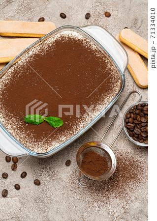 Traditional Italian Tiramisu dessert in glass baking dish and savoiardi cookies on concrete background Traditional Italian Tiramisu dessert in glass baking dish and savoiardi cookies on concrete background 71334010