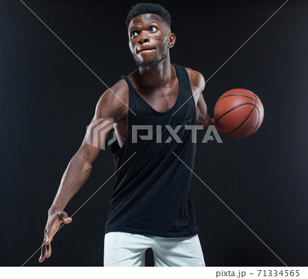 Portrait of afro american male basketball player playing with a ball over black background. Fit young man in sportswear holding basketball 71334565
