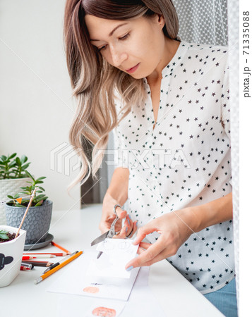 Woman decorates flower pots with handmade decorations for Halloween. Painted ghost in medical protective mask and pumpkin in flower pot with succulent plant. 71335088