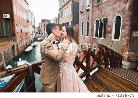 Romantic, fairytale, happy newlywed couple hugging and kissing in a park, trees in background 71336775