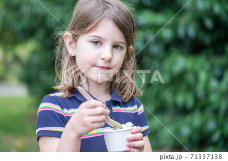 A cute little girl enjoys ice cream in park A cute little girl enjoys ice cream in park 71337138