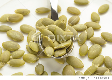 Peeled pumpkin seeds on a dessert spoon in a white plate 71338563