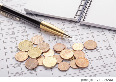 Many euro coins on the old black wooden table. Pen, notebook and accounting documents. The concept of dependence of expenses on profit 71339288