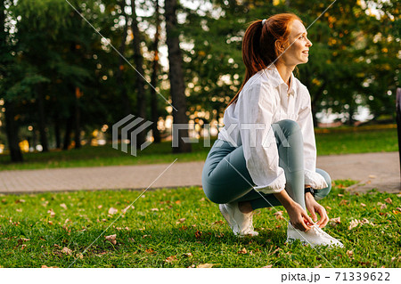 Side view og cheerful red-haired young woman tying shoelaces on sneakers before running. Side view og cheerful red-haired young woman tying shoelaces on sneakers before running. 71339622