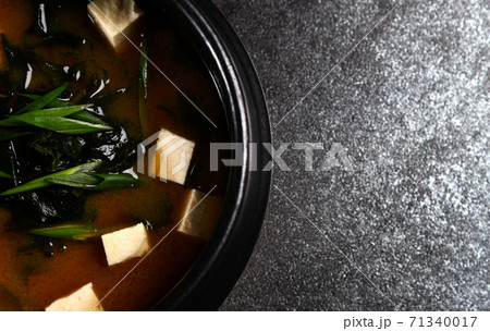 Japanese miso soup in a black bowl with tofu and fresh onion on rustic stone background closeup 71340017