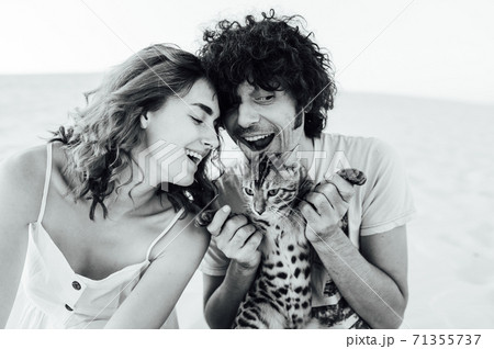 A handsome man with curly hair gently hugs his beloved. They have a cat in their hands A handsome man with curly hair gently hugs his beloved. They have a cat in their hands 71355737