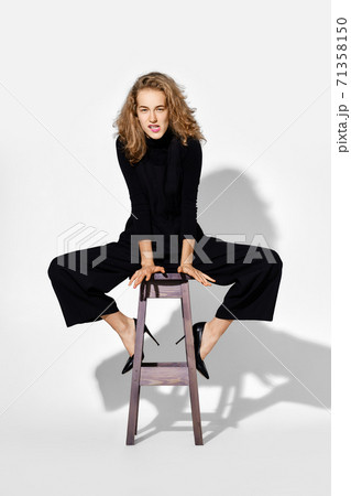 Tricky young woman sits on tall chair 71358150