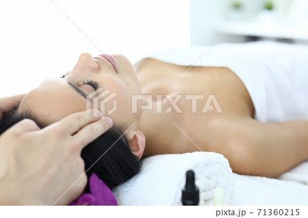 Woman lies on massage table with her eyes closed masseur does an acupressure face massage 71360215
