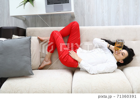 Woman lies on couch and drinks alcohol from bottle. 71360391
