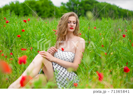 A young long-haired girl enjoys the colors of nature on a blooming poppy field on a hot summer day A young long-haired girl enjoys the colors of nature on a blooming poppy field on a hot summer day 71365841