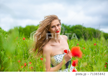A young long-haired girl enjoys the colors of nature on a blooming poppy field on a hot summer day 71365842