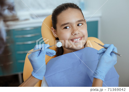 African american doctor in rubber gloves with stomatology tool for treats tooth of smiling little child African american doctor in rubber gloves with stomatology tool for treats tooth of smiling little child 71369042