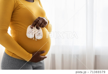 Closeup of baby shoes on pregnant black lady belly Closeup of baby shoes on pregnant black lady belly 71369379