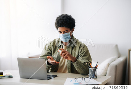 Distance education during coronavirus. Black teen student in medical mask applying antiseptic near laptop at home 71369556