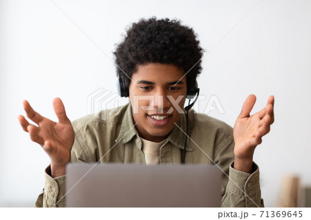 Web based education concept. Happy black teen student in headset talking to his college tutor online on laptop, indoors 71369645