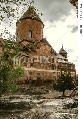 The reverse side of the medieval Church of the blessed Holy Virgin with a bell tower among trees and basalt boulders in the spring rain 71371380