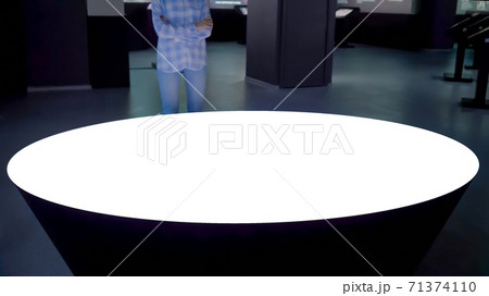 Woman looking at blank white display of round table kiosk - white screen concept 71374110