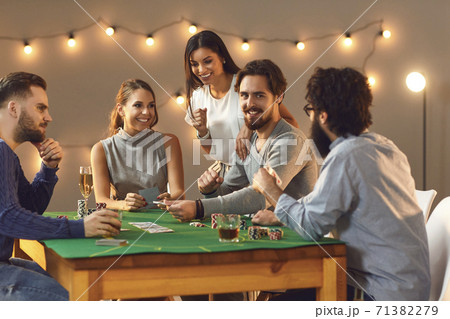 Happy friends betting, playing poker gambling on table with drinks at home 71382279