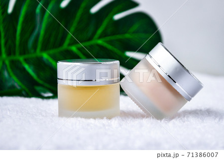 Glass jar with cream organic body care cosmetic products on monstera palm leaves over white textile background. SPA branding mock-up. 71386007