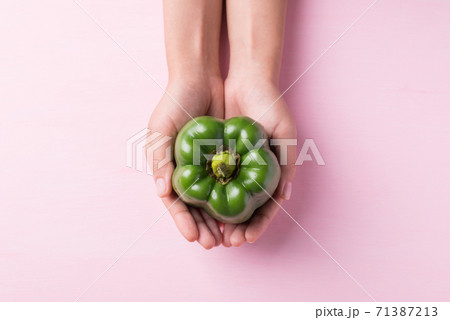 Green bell pepper holding by hand on pink background 71387213