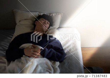 ベッドで寝ている若い男性 71387483