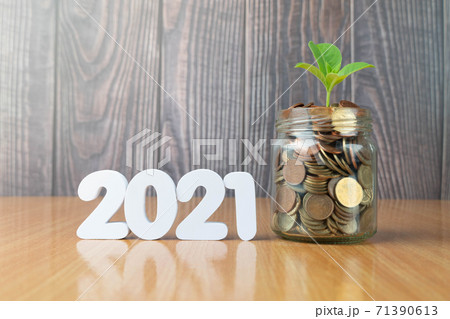 New year saving money and financial planning concept. Plants growing on glass of coins or piggy bank with 2021 number on wooden table. Idea for business growth and investment. 71390613