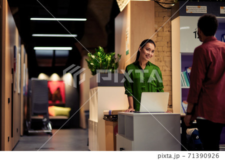 Young cheerful asian woman talking with colleague while standing together in corridor of the modern office Young cheerful asian woman talking with colleague while standing together in corridor of the modern office 71390926