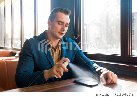 Young caucasian guy businessman in a blue suit sprays an antiseptic on a mobile phone 71394078