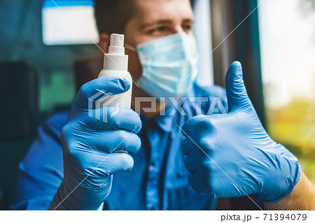A man on the background in a protective mask holds an antiseptic in his hand in medical gloves and shows a cool thumb up 71394079