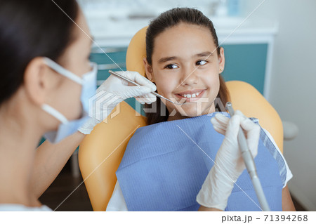 Millennial female doctor in protective mask and glove holds medical instrument and checks oral cavity 71394268