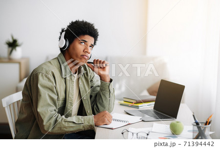 Pensive black teen in headphones passing difficult exam on laptop, thinking about his answer at home, space for design 71394442