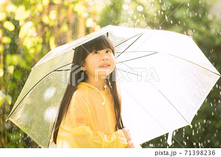 レインコートを着て公園で雨を遊ぶ小さい女の子の写真素材