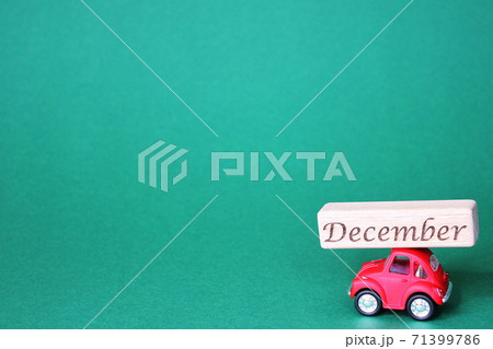 A small red toy car carrying a wooden block with the inscription December on its roof. 71399786