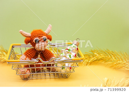 The bull is the Symbol of the new year 2021. Knitted toy bull and a toy Christmas tree are in a supermarket toy cart The bull is the Symbol of the new year 2021. Knitted toy bull and a toy Christmas tree are in a supermarket toy cart 71399920