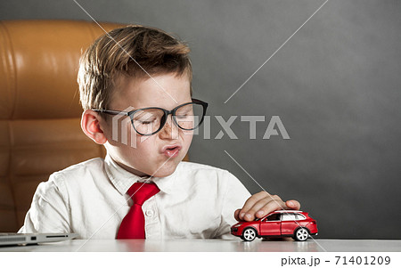 Little businessman playing with red toy car. Child boy dreams about car. Business school for children. 71401209