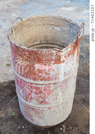 An old rusty metal barrel covered with multi-colored spots stands on the street. Everything for repair, construction. 71403107