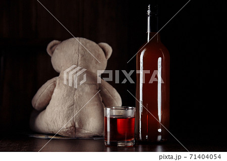 Alcohol and child abuse. Teddy bear as a symbol of child's safety and bottle with glass close-up 71404054