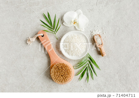 Spa concept. Natural Organic spa cosmetics products, sea salt, massage brush and tropic palm leaves on gray marble table from above. Spa background Spa concept. Natural Organic spa cosmetics products, sea salt, massage brush and tropic palm leaves on gray marble table from above. Spa background 71404711