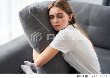 Woman sitting on couch and holding her pillow Woman sitting on couch and holding her pillow 71407763