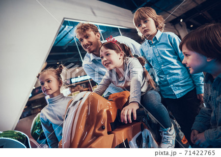 Dad and children watch as girl drives motorcycle. Dad and children watch as girl drives motorcycle. 71422765