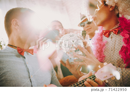 People stand at a gay party with a disco ball. 71422950