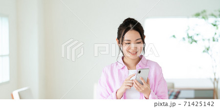 リビングでスマホを操作する笑顔の若い女性 バナーサイズ リビングでスマホを操作する笑顔の若い女性 バナーサイズ 71425142