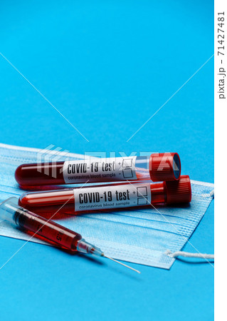 Syringe, test tube with blood sample and disposable face mask to prevent COVID-19 virus on blue background 71427481