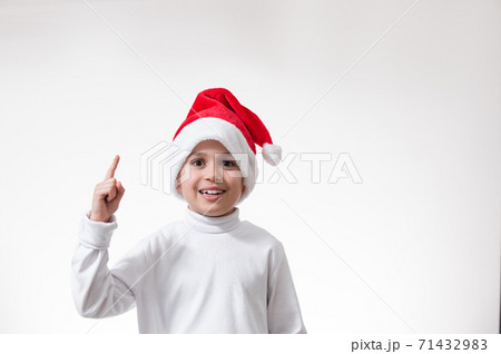 The boy in the red santa hat smiles and points his finger up. Christmas concept. 71432983